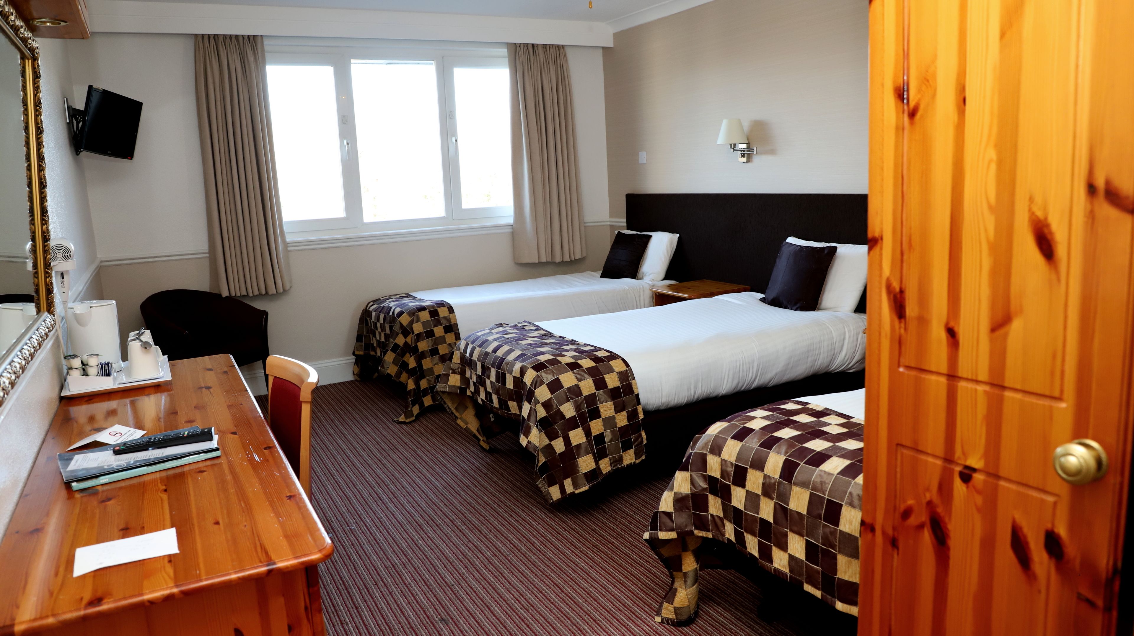 Une chambre d’hôtel comprenant un lit, deux tables de chevet, un bureau avec une chaise, un téléviseur fixé au mur et une fenêtre avec des rideaux.