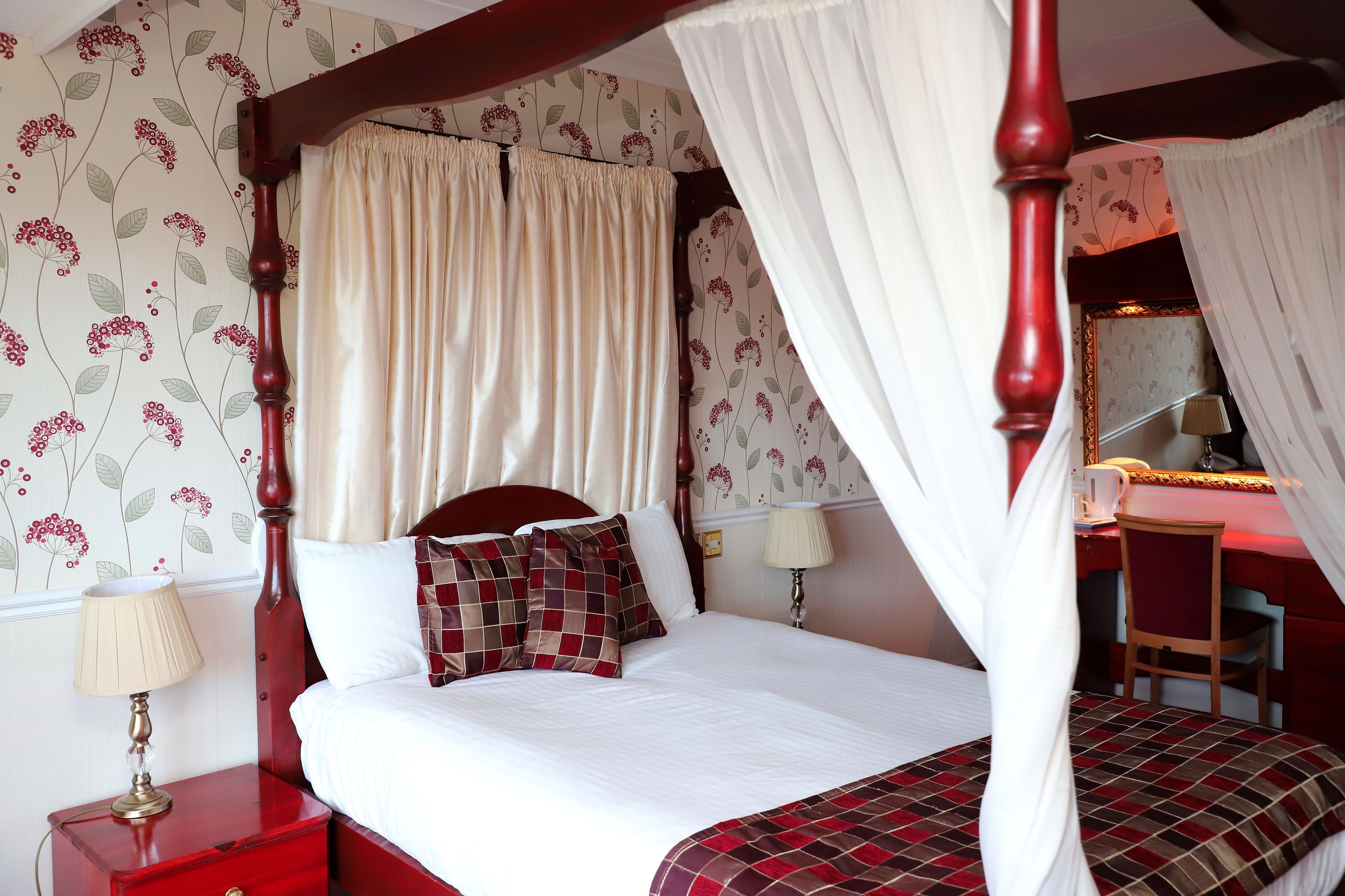 A four-poster bed with a canopy, a desk with a chair, and a nightstand with a lamp.