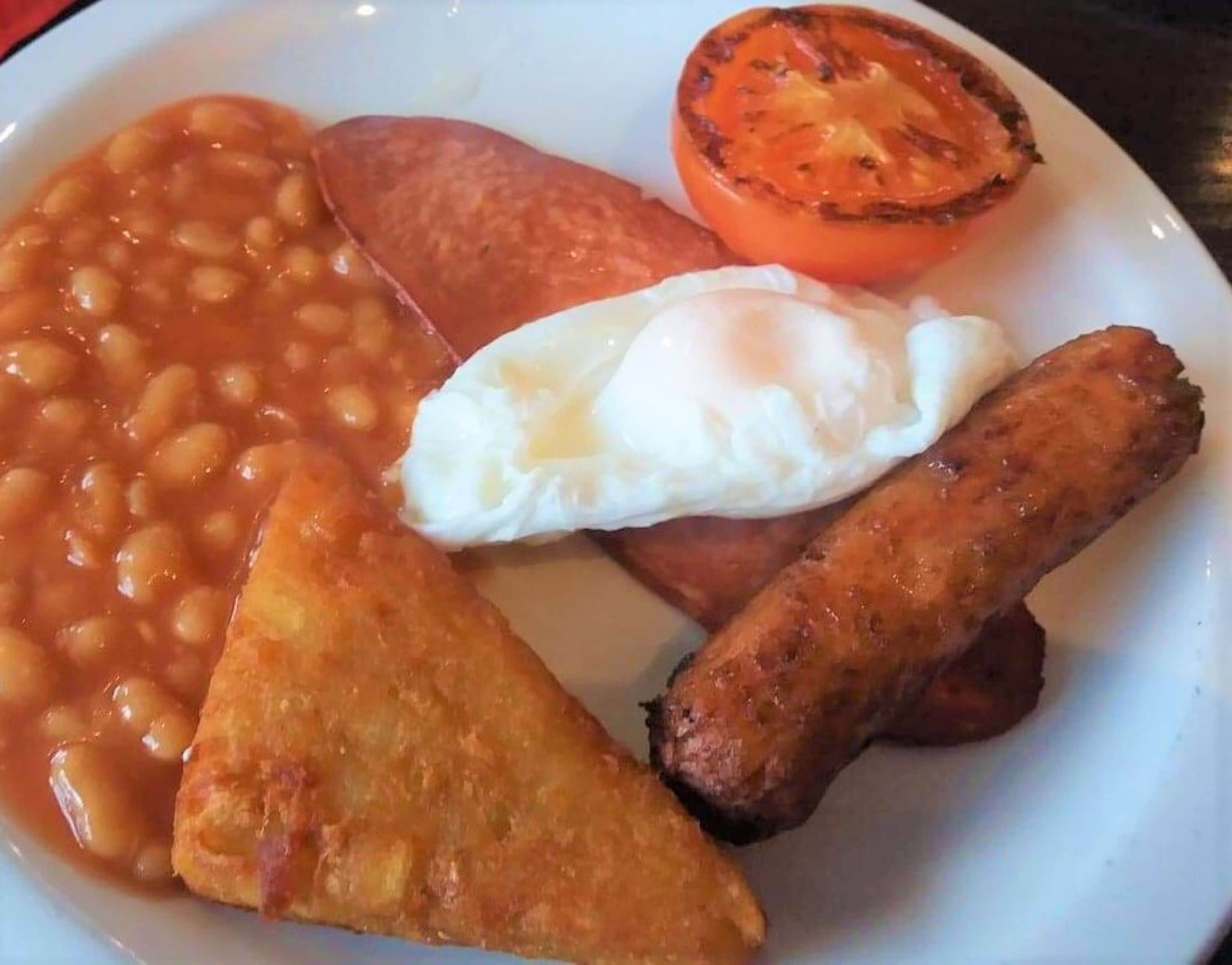 A plate with beans, a fried egg, a grilled tomato, and sausages.