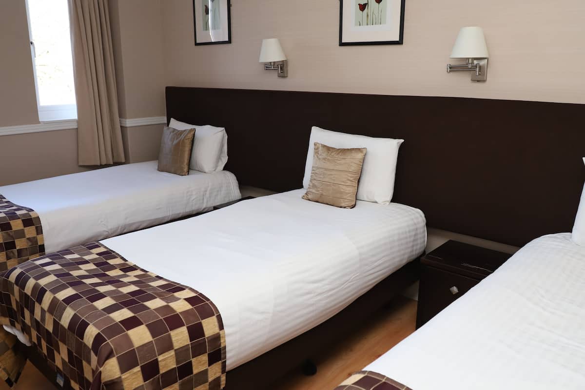A hotel room with two beds, each with a checkered bedspread and white linens. There are wall-mounted lamps and framed artwork on the wall.