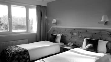 A hotel room with two beds, a window with curtains, a wall-mounted lamp, and a telephone on the nightstand.