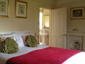 Un dormitorio con cama, una puerta blanca, un baño con lavamanos y una chimenea.