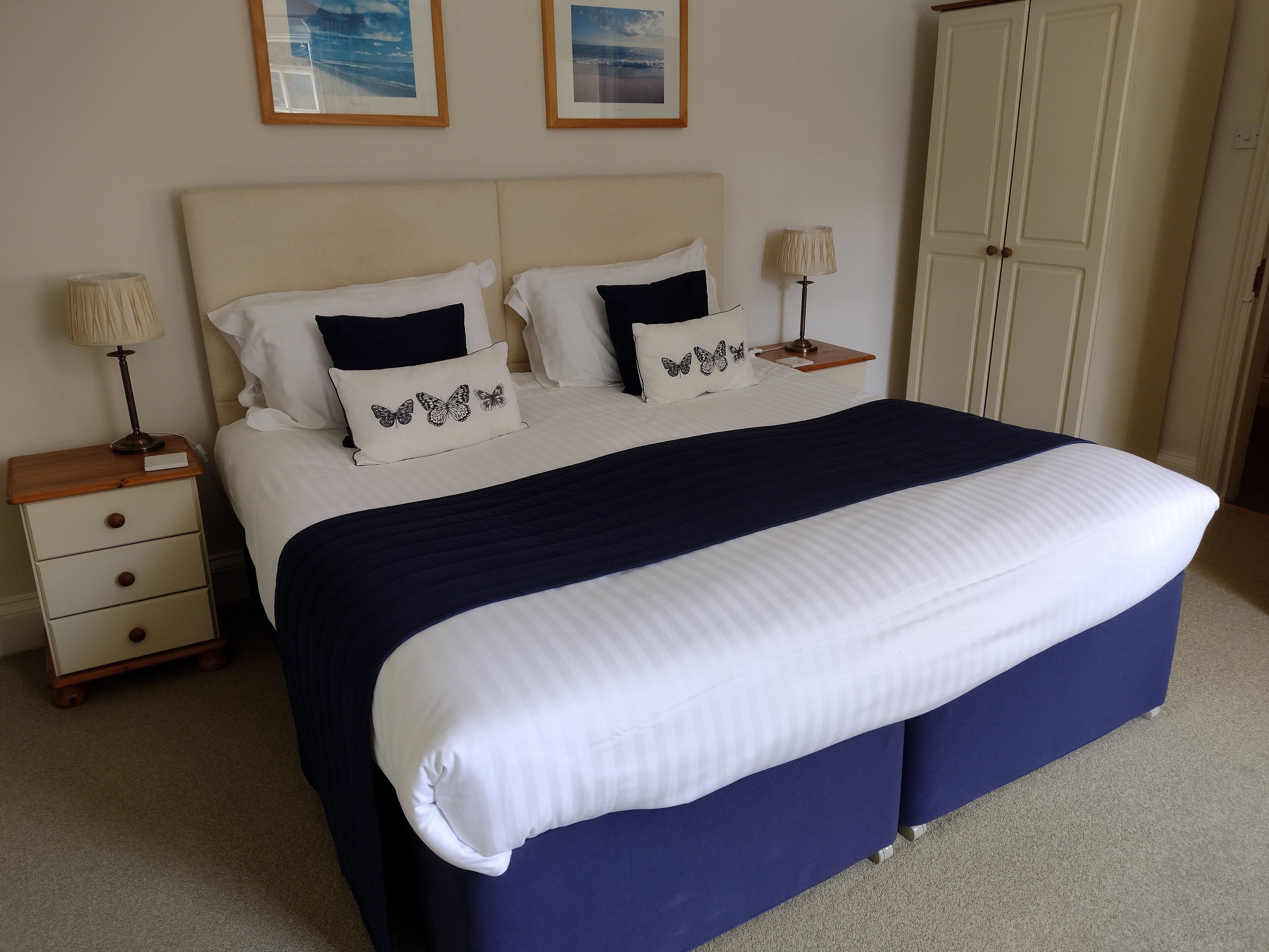 A neatly made bed with a white and navy blue bedspread, two bedside tables with lamps, and a wardrobe.