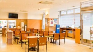 A spacious indoor area with multiple tables and chairs, a reception desk, and a television screen on the wall. - Toyoko Inn Miyazaki Ekimae (MIYAZAKI)
