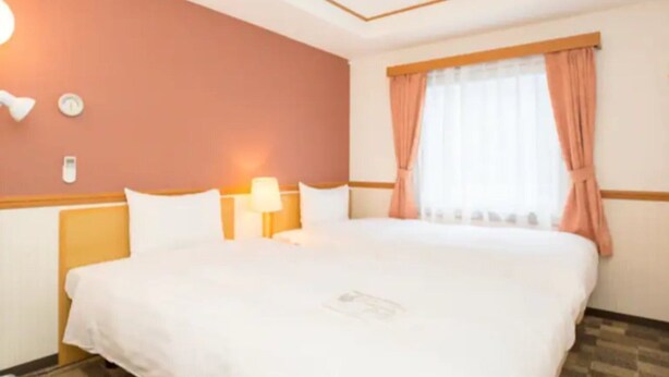 A hotel room with a large bed, a bedside table with a lamp, a window with curtains, and a wall clock. - Toyoko Inn Miyazaki Ekimae (MIYAZAKI)