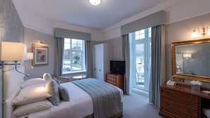A hotel room with a bed, a television, a dresser, a mirror, and a window with curtains. - The Belmont (Sidmouth)