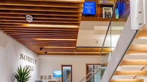 A modern interior with a wooden ceiling, a reception desk, a staircase, and a view of a pool. - The Belmont (Sidmouth)