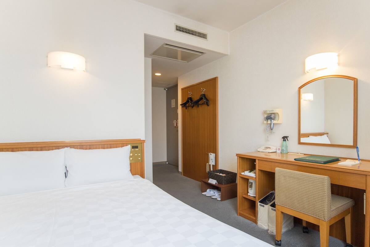 Una habitación de hotel con cama, escritorio, silla, espejo y puerta que da a otra habitación.