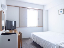 Habitación de hotel con cama, escritorio con televisor, silla, refrigerador pequeño y ventana con persianas.