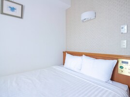 Een hotelkamer met een bed, een aan de muur bevestigde lamp en een thermostaat.
