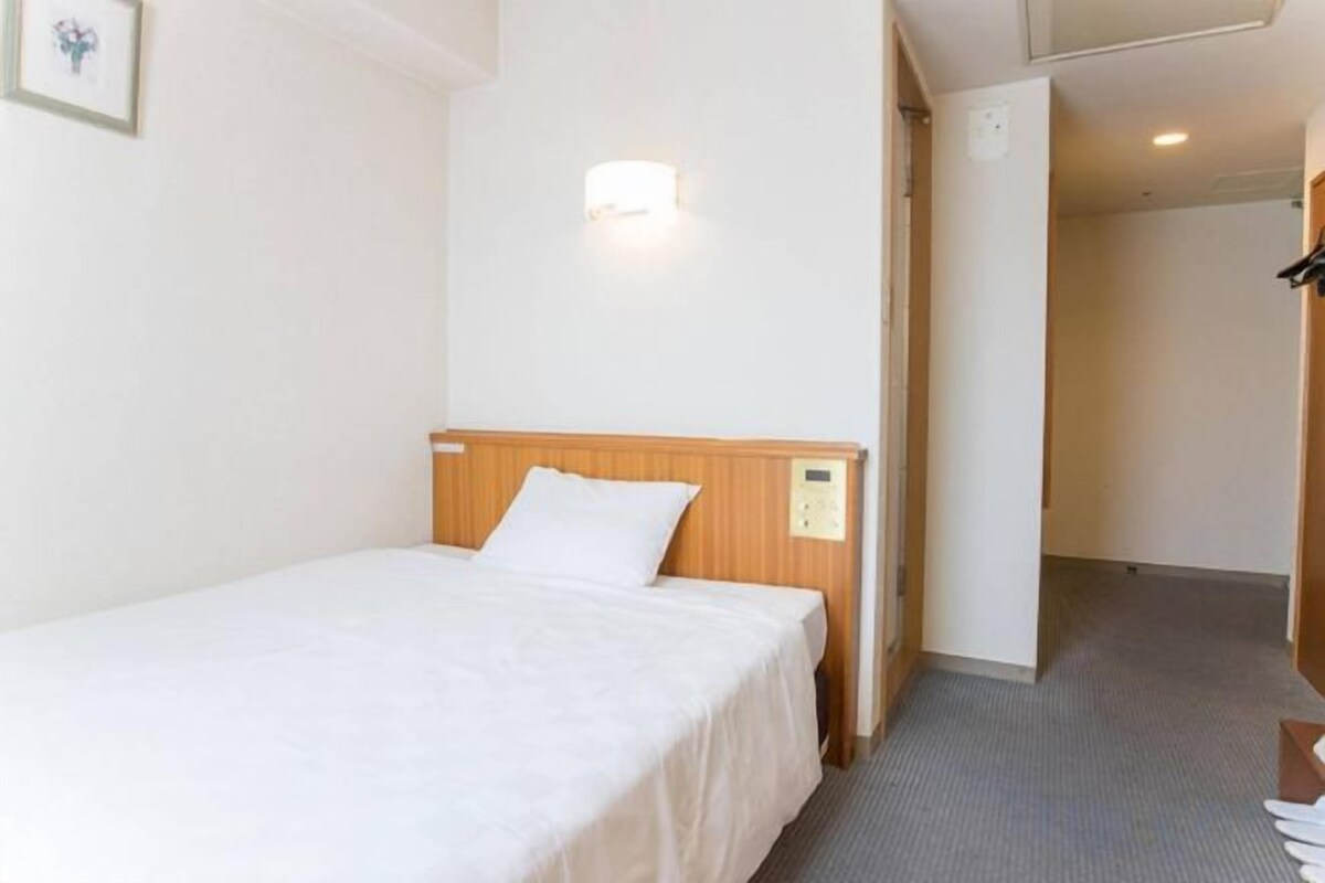 A hotel room with a single bed, a wooden headboard, a wall-mounted light, and a carpeted floor.