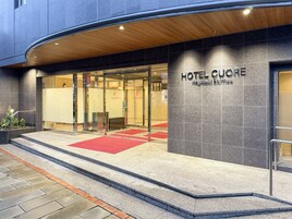 Exterior del Hotel Cuore con un diseño moderno, destacando una entrada imponente con puertas de vidrio y una alfombra roja que conduce a ella.