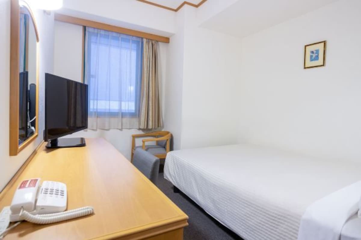 Een hotelkamer met een houten bureau, een bed, een televisie en een telefoon.