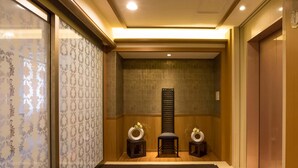 A hallway with patterned wallpaper, a wooden bench, two small side tables with floral arrangements, and a wall-mounted panel.