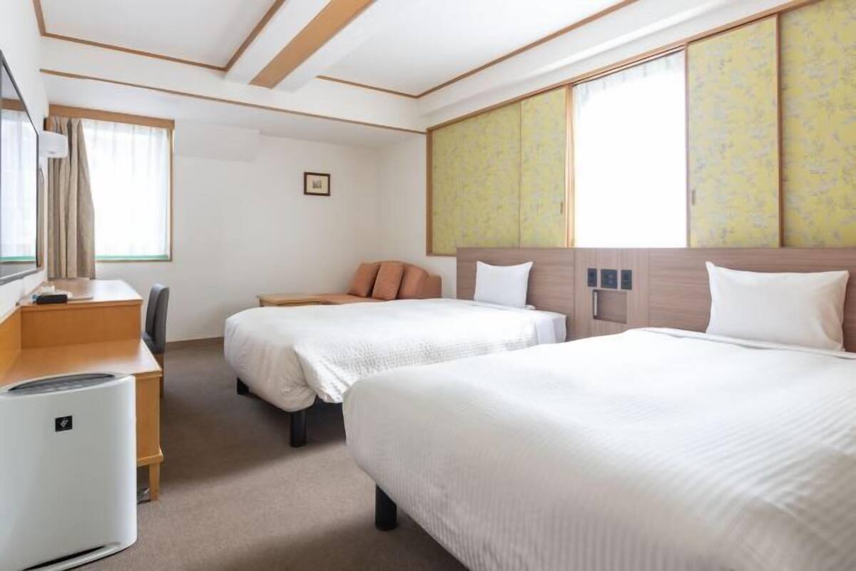 Een hotelkamer met twee bedden, een bureau, een stoel, een verwarming en een groot raam met uitzicht.