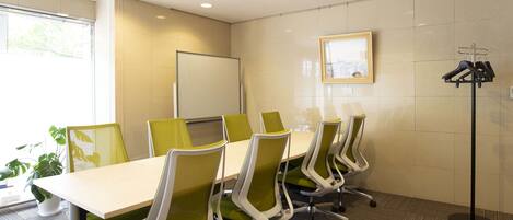 A conference room with a long table, green chairs, a whiteboard, and a coat rack.