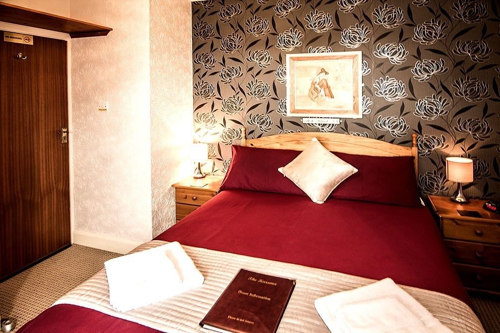 Een hotelkamer met een groot bed, een houten hoofdbord, een nachtkastje met een lamp en bloemenbehang.