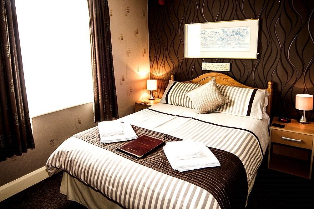 A hotel room with a bed, bedside tables, a lamp, a framed picture on the wall, and a window with curtains.