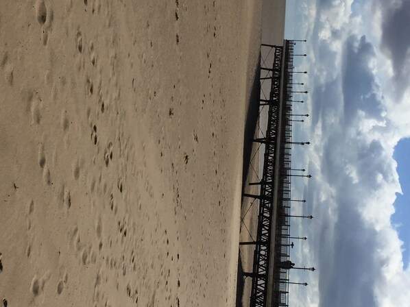 Una playa con huellas en la arena y un muelle al fondo.