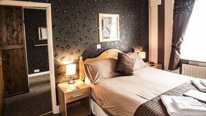Une chambre d’hôtel avec un lit, une table de chevet, une lampe, un tableau encadré au mur et une fenêtre avec des rideaux.