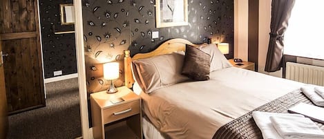 A hotel room with a bed, a nightstand, a lamp, a framed picture on the wall, and a window with curtains.