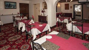 Un espace repas avec des tables recouvertes de nappes rouges, des chaises en métal noir et des tapis à motifs.