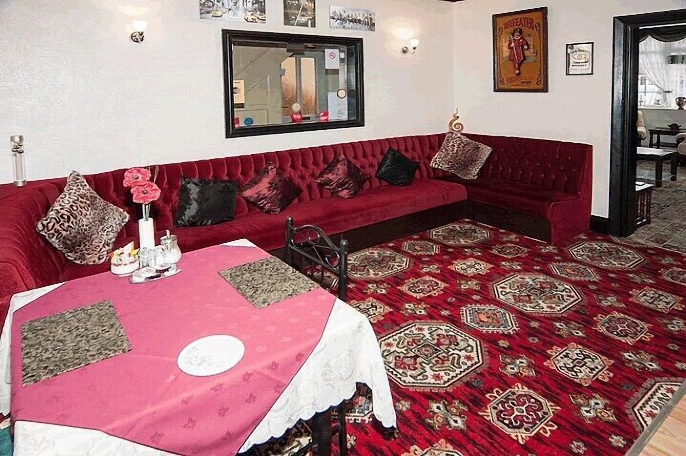 A room with a red sofa, a table with a red tablecloth, and a patterned carpet.