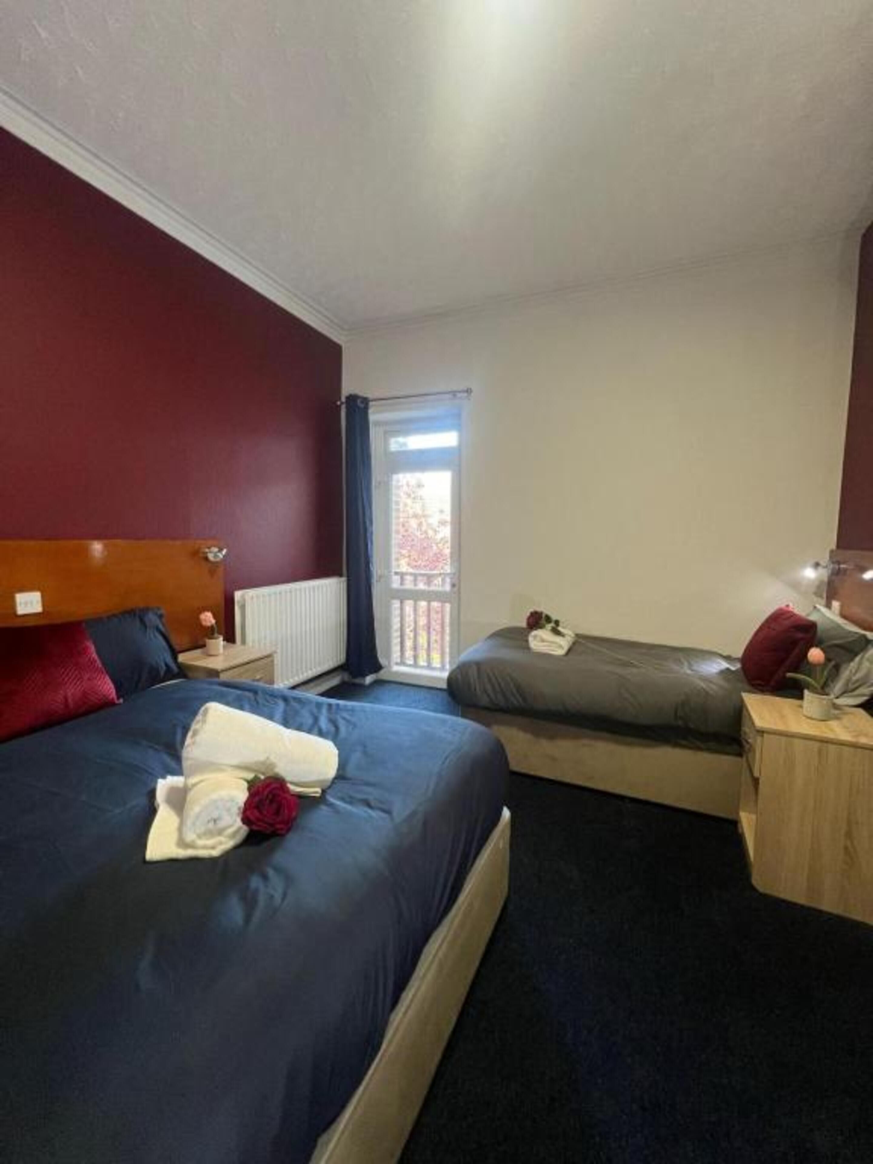 A hotel room with a large bed, a smaller bed, a nightstand, a lamp, and a view of the outside.