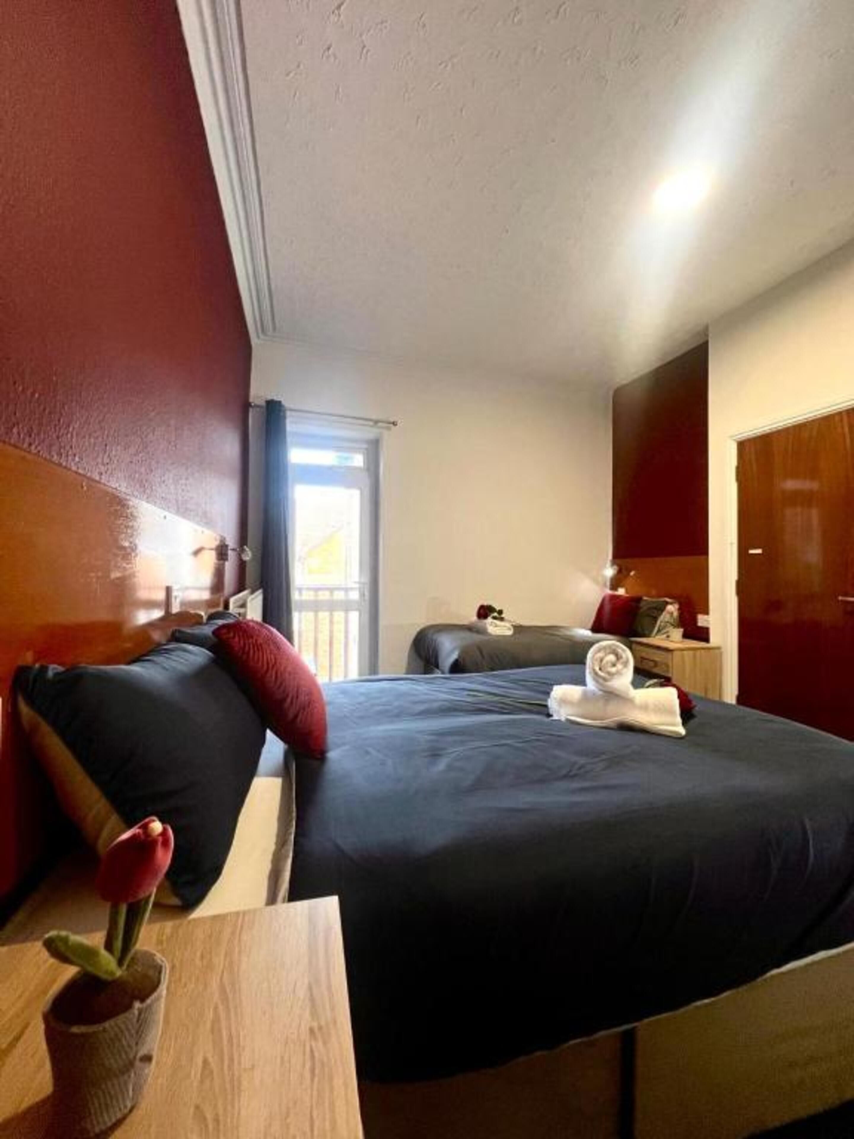 A hotel room with a large bed, a small table with a plant, and a window with curtains.