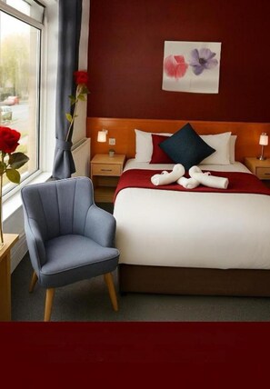 A hotel room with a bed, a chair, a nightstand, a window with a view, and a wall with a floral painting. - OYO Diamond Apartments Skegness (Skegness)