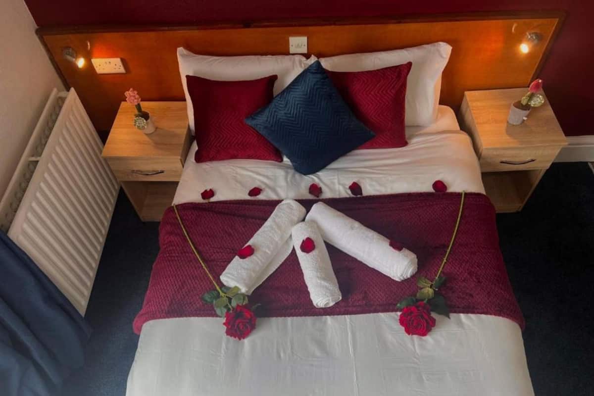 A neatly made bed with rose petals and towels arranged in a fan shape.