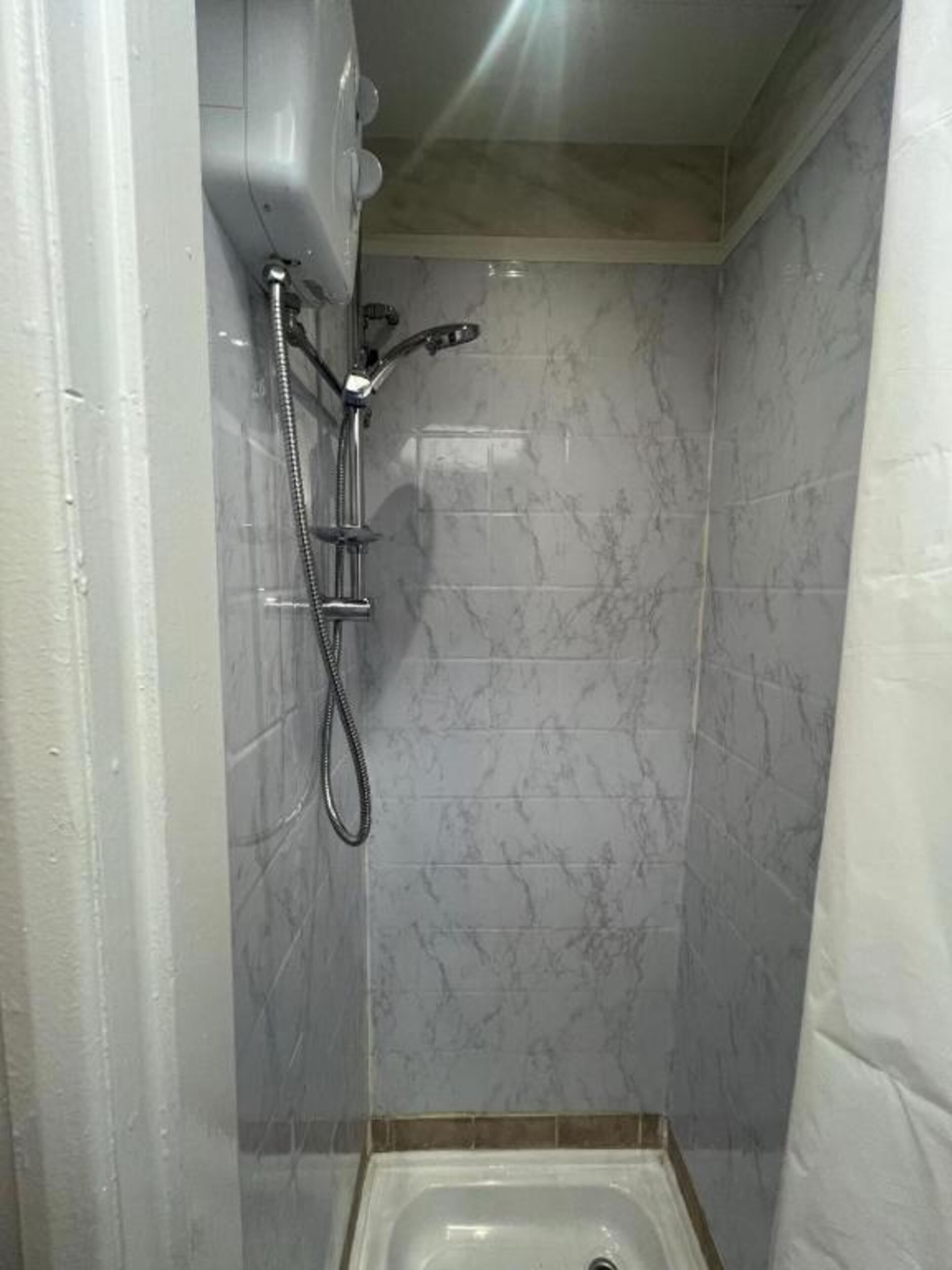 A small, tiled shower area with a handheld showerhead and a drain.