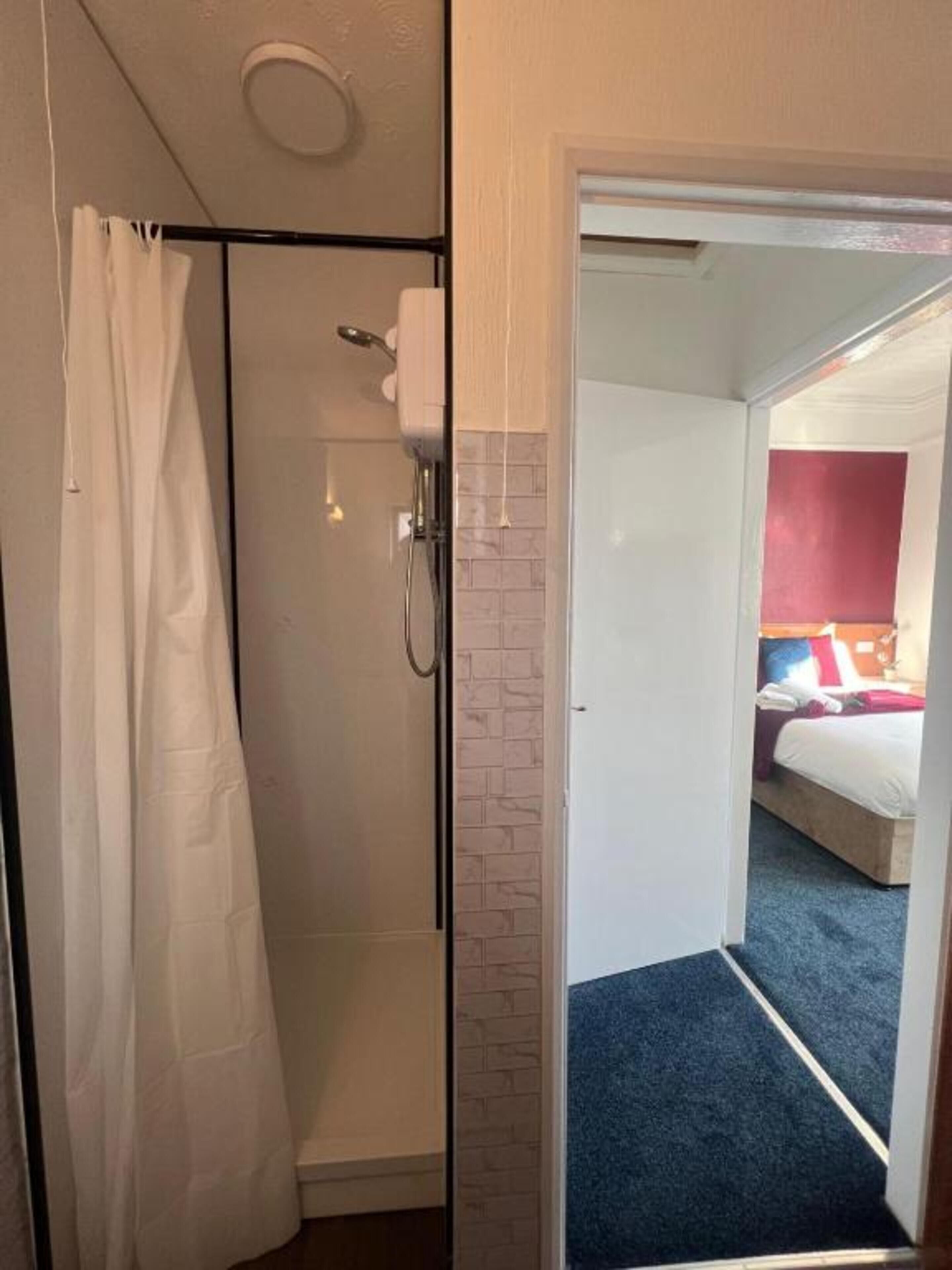 Una camera d'albergo con doccia, un letto e vista sul corridoio.