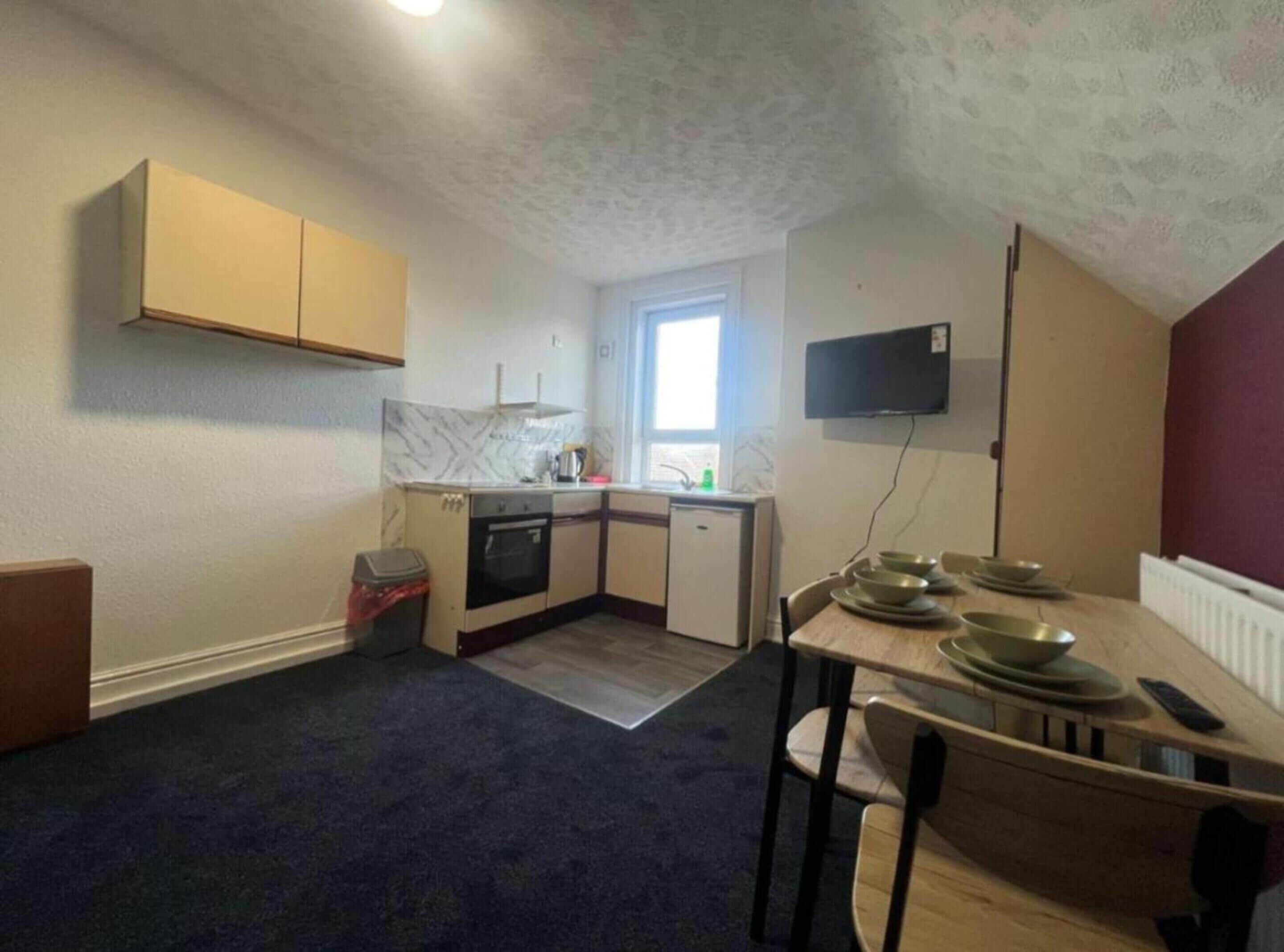 A compact kitchen with a window, a built-in oven, a sink, and a television mounted on the wall.