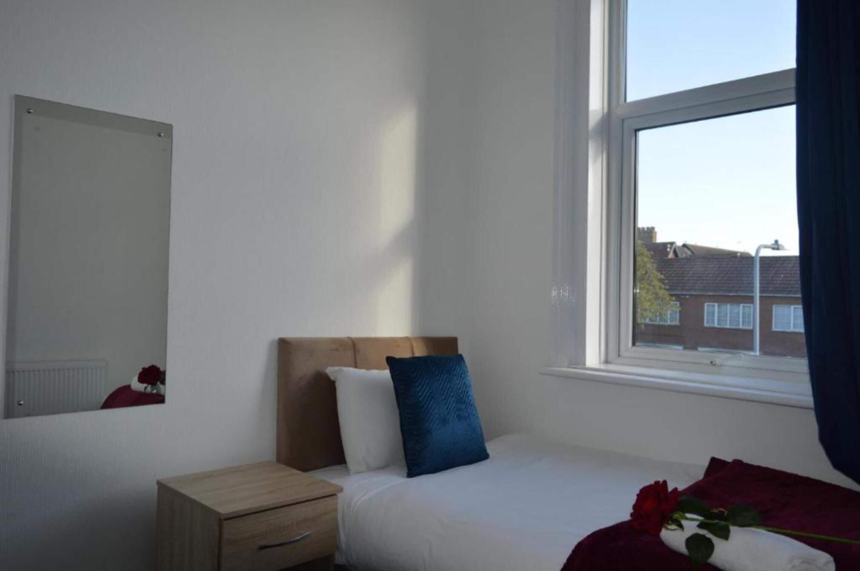 A bedroom with a bed, a nightstand, a mirror, and a window with a view of buildings.