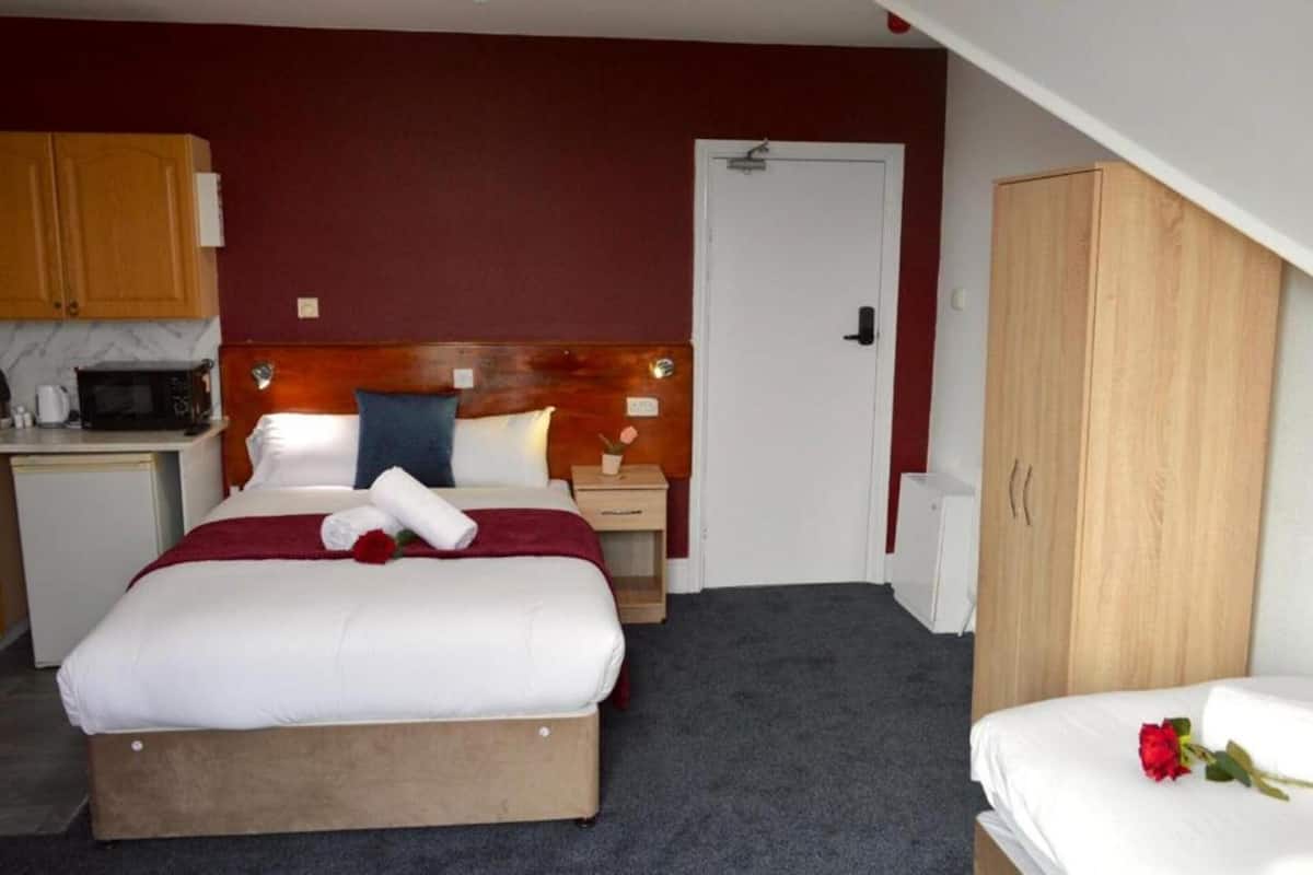 A hotel room with a bed, a wooden wardrobe, a small kitchenette, and a door.