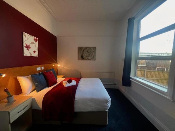 A hotel room with a bed, bedside table, and a window with a view of a fence. - OYO Diamond Apartments Skegness (Skegness)
