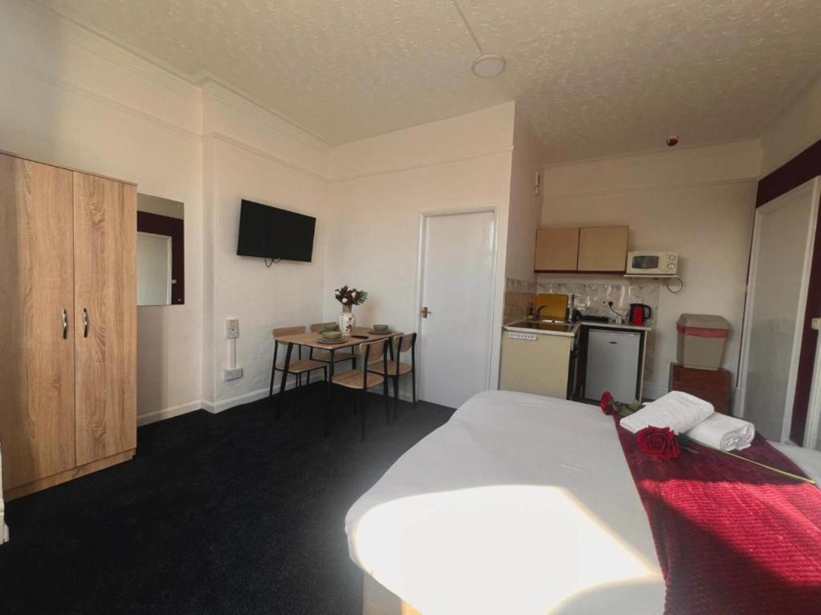 A hotel room with a bed, a desk with a chair, a small kitchenette, and a wardrobe.
