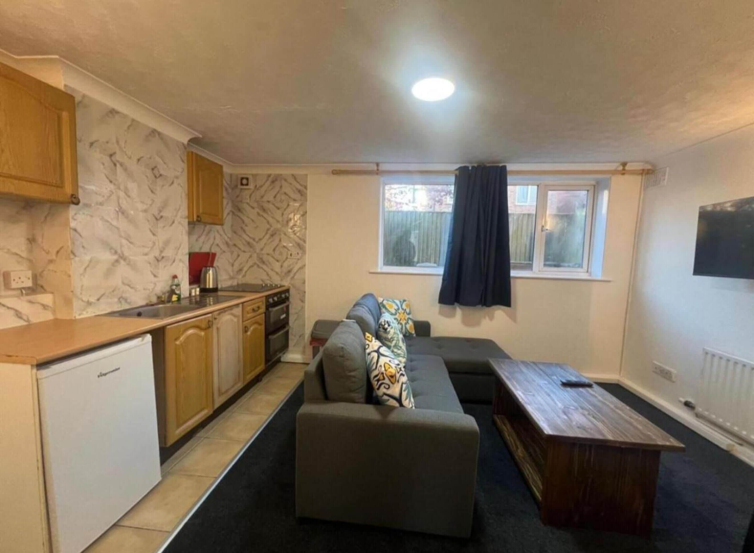 A compact living space with a kitchenette, a sofa, a coffee table, and a window with curtains.