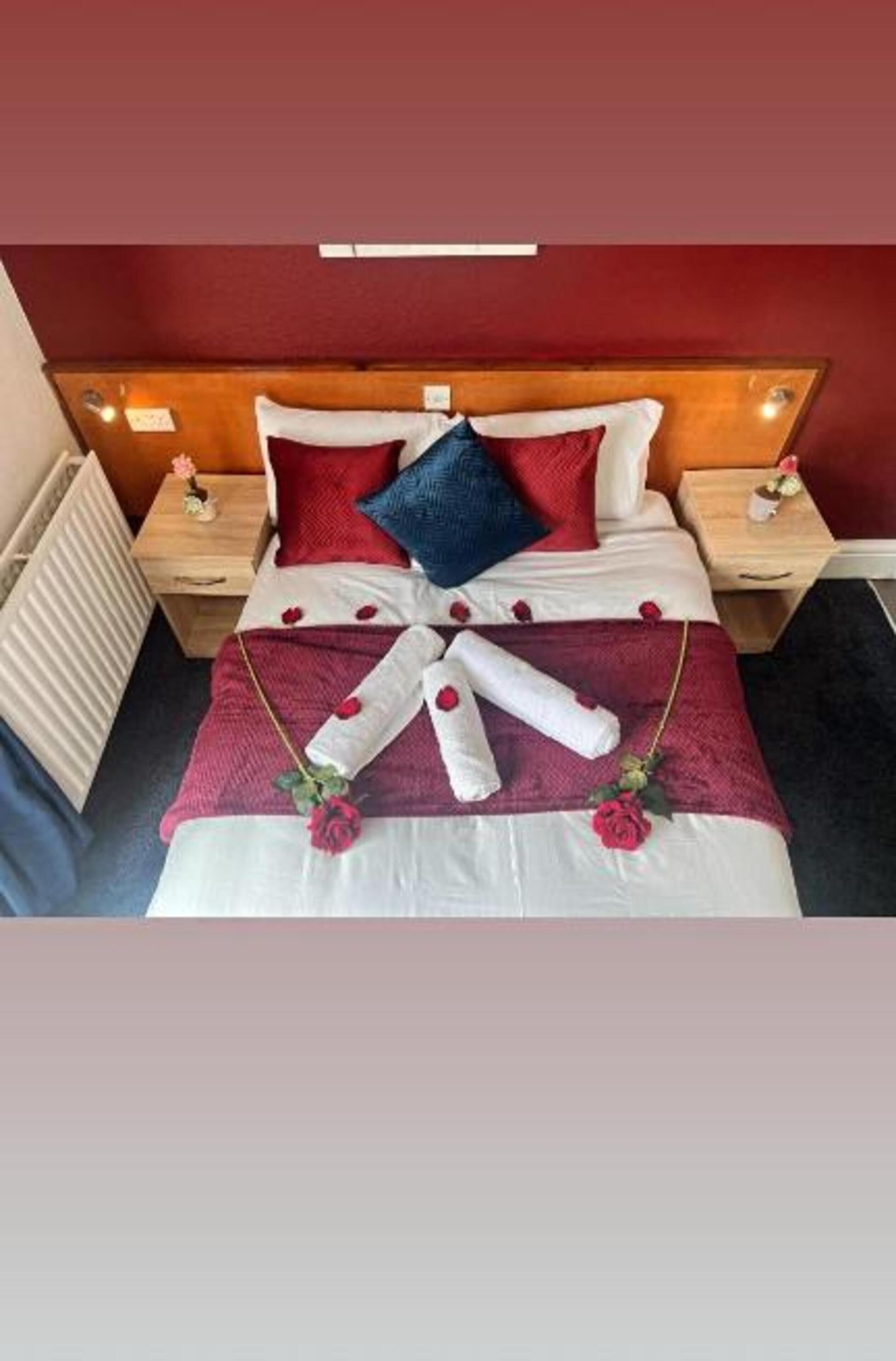 A neatly made bed with a red and white color scheme, a wooden headboard, and a bedside table with a small vase.