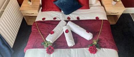 A neatly made bed with a red and white color scheme, a wooden headboard, and a bedside table with a small vase.