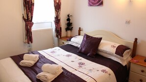 A neatly made bed with a floral bedspread, a bedside table with a lamp, and a window with curtains. - The Homestar (Skegness)