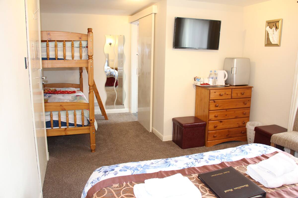A bedroom with a bunk bed, a dresser, a television, and a small table with a kettle and cups.