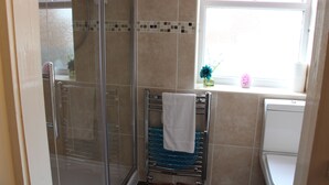 A bathroom with a glass-enclosed shower, a towel rack with a white towel, and a window with a pink curtain. - The Homestar (Skegness)