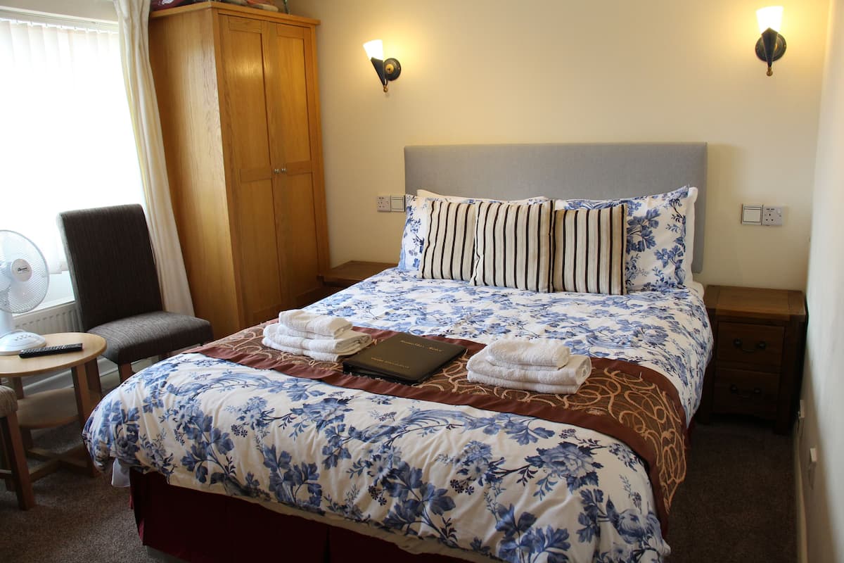 A neatly made bed with a floral bedspread, two bedside lamps, and a wooden wardrobe.