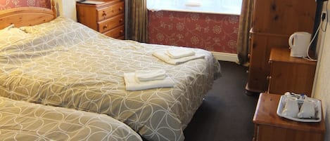 Habitación de hotel con dos camas, un armario de madera, un escritorio con tetera y una ventana con cortinas.