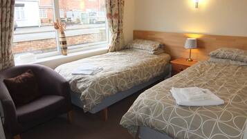 A hotel room with two beds, a chair, a window with curtains, and a lamp.