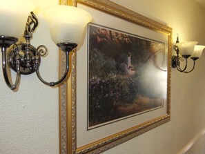A framed painting of a woman in a garden, flanked by two wall sconces with white shades. - The Monsell Hotel (Skegness)