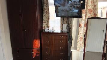 A room with a large wooden wardrobe, a small wooden dresser, a television mounted on the wall, and a door with a cross symbol.
