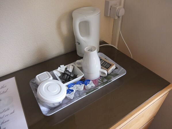 Una cafetera, un jarro de leche y una bandeja con sobres de leche sobre una encimera.